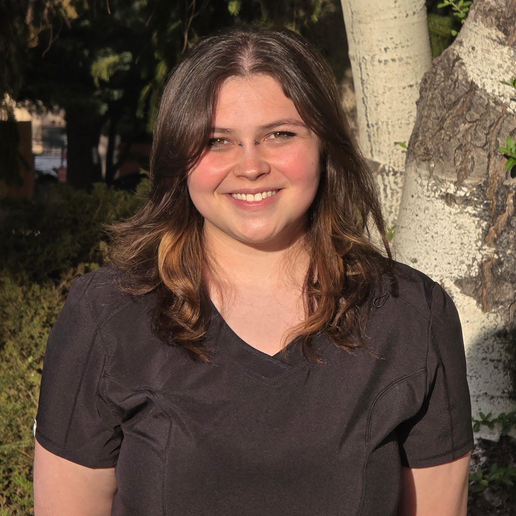 Sky Elizondo, smiling, photographed outdoors in dark scrubs in front of an aspen tree.